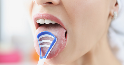 woman scraping her tongue as part of her oral care cleaning technqiues